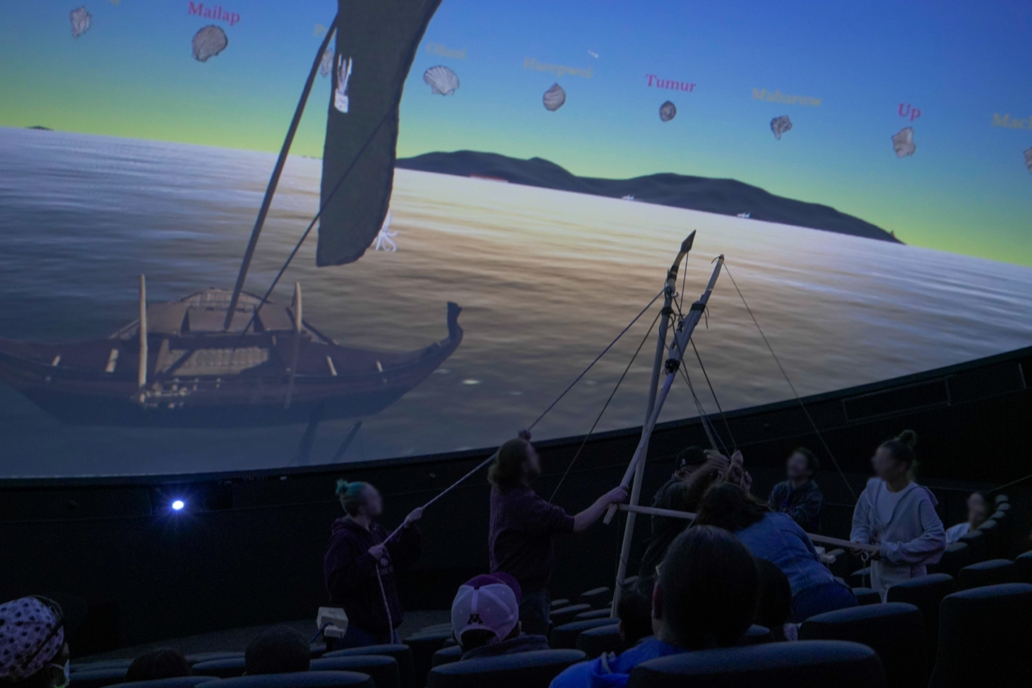 image of a planetarium audience looking at an image of a canoe with a sail