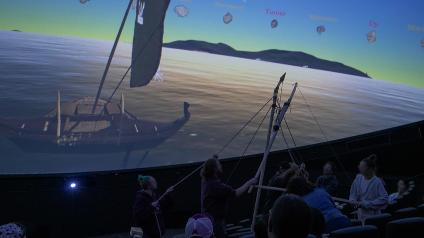 image of a planetarium audience looking at an image of a canoe with a sail